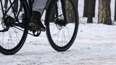 An alone woman cyclist rides by a landscape woodland trail, slow motion. Young woman rides a bike on a snowy path between winter trees in a pine forest. Countryside, healthy lifestyle, hobbies, sport