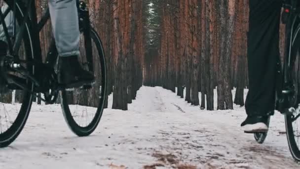 雪の木の間の冬の道に沿って2台の自転車に乗って一緒にカップルの低ビュー 女と男の自転車は自然道をたどります 自転車で2人の自転車旅行 ライフスタイル スポーツ — ストック動画