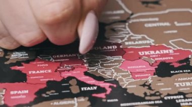 Female Hand Scratching Europe countries on the Surface of Scratch World Map. Scratch map with world countries, close-up. Scratching visited countries on the travel map. Erase country on scratch map