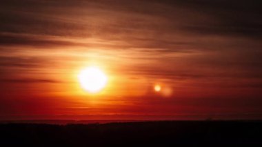Timelapse of sunset with a lens flare in the orange sky with soft clouds over the horizon. Big bright red sun with sunrays moves down. Awesome epic cloud space, vibrant color. Time Lapse. Sundown