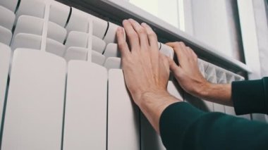 Erkek avuçları duvardaki soğuk ısıtıcı kalorifere değiyor. Mans eller evin ısıtma sistemi üzerinde sıcak tutmaya çalışıyor. Kötü ısıtma sistemi kavramı, dairede soğuk, kış mevsimi.