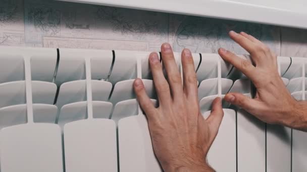 男の手は家の暖房システムに暖かく保つことを試みている 男性の手のひらは壁に対して冷たい加熱ラジエーターに触れる 貧しい暖房システムの概念 アパートで寒い 冬の季節 — ストック動画