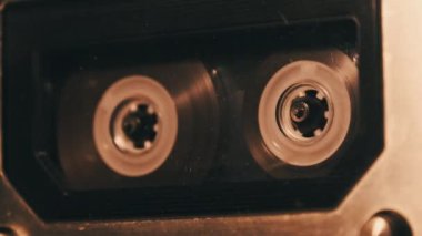 Retro bir teypte ses kaydı oynatılıyor. Plak çalar titreyen mum ışığında eski şeffaf bir ses kaseti çalıyor, yakın plan. Eski bant makaraları güvertede dönüyor. Kaydı ara, oynat