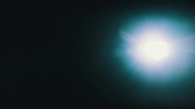 Siyah arkaplanda kameraya doğrultulmuş parlak bir el fenerinin ışığı. Işığın bir yandan diğerine soyut hareketi. Lenslerdeki ışık yansımalarının yansıması. Lens yanıyor, ışık sızıyor.