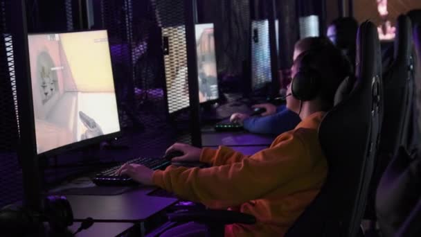 若いゲーマーはプロのゲームチェアに座って Eスポーツクラブでビデオゲームをプレイします ネオンライト付きのコンピュータクラブのヘッドセットの少年は ビデオゲームに焦点を当てています ゲームクラブの10代の若者趣味 — ストック動画