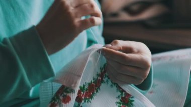 Güzel kadın elleri iplik ve iğneyle elle dikilmiş. Genç bir kadın rahat bir kanepede ev kıyafetleri içinde otururken dikiş diker. Ev atmosferi ve pencereden gelen güneş ışığı. Yaşam tarzı, el yapımı. 4K