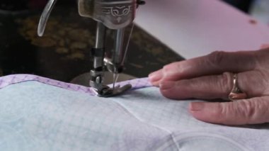 An aged seamstress sews at a traditional sewing machine at home in slow motion. Close-up of aged female hands working at a retro sewing machine. The needle quickly moves up and down. Lifestyle, hobby