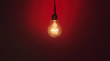Koyu kırmızı arka planda parlak ve yanıp sönen bir lamba. Edison ampulü yavaşça açılıp kapanıyordu. Yakından yanıp sönüyordu. Ilık yanıp sönen filament. Retro klasik ampul. Boşluğu kopyala, metin için yer