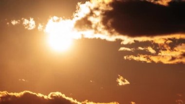 Turuncu gökyüzünde kümülüs bulutlarıyla muhteşem bir gün batımı, Timelapse. Parlak turuncu güneş stratus bulutlarının arkasına doğru hareket ediyor. Destansı bulut uzayı, canlı bir renk. Zaman aşımı. Bulutlu bir gökyüzünde güzel bir gün batımı.