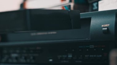 Insert VHS cassette into VCR player. Black vintage videotape cassette recorder on a desk with many archived video cassettes. Male hand inserting old VHS Tape into a retro player. Home video, nostalgia