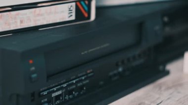 Insert VHS cassette into VCR player. Black vintage videotape cassette recorder on a desk with many archived video cassettes. Male hand inserting old VHS Tape into a retro player. Home video, nostalgia