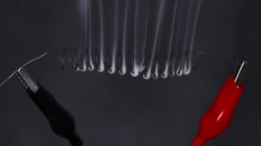 Nichrome wire heats up to red with smoke under a high electric current, slow motion. Nichrome filament in the form of spiral connected to power wires. Close-up, high metal resistance. Current strength