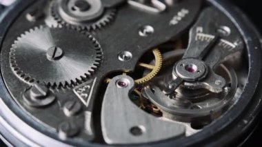 The mechanism of vintage stopwatch rotates close-up. Round clock watch mechanism working in a macro. Old retro clockwork gears, cogwheels, and pendulum movement inside the ancient clock. 4K