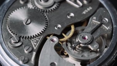 The mechanism of vintage stopwatch rotates close-up. Round clock watch mechanism working in a macro. Old retro clockwork gears, cogwheels, and pendulum movement inside the ancient clock. 4K