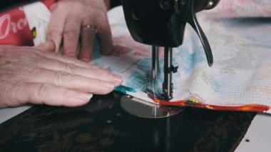 Old female hands of seamstress sew at a retro sewing machine at home in slow motion. Close-up of aged female fingers sewing fabric at a traditional sewing machine. The needle quickly moves up and down