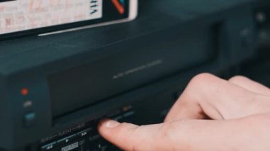 Eject VHS tape cassette from VCR player. Male hand pushes a button and pulls out VHS from vintage videotape recorder on desk with many archived video cassettes. VHS retro player. Home video, old tape