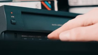 Eject VHS tape cassette from VCR player. Male hand pushes a button and pulls out VHS from vintage videotape recorder on desk with many archived video cassettes. VHS retro player. Home video, old tape