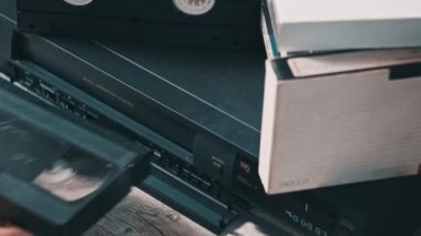 Insert VHS cassette into VCR player. Black vintage videotape cassette recorder on a desk with many archived video cassettes. Male hand inserting old VHS Tape into a retro player. Home video, nostalgia