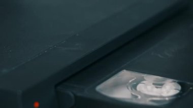 Insert VHS cassette into VCR player. Black vintage videotape cassette recorder on a desk with many archived video cassettes. Male hand inserting old VHS Tape into a retro player. Home video, nostalgia