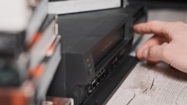 Eject VHS tape cassette from VCR player. Male hand pulls out VHS from a vintage videotape recorder on a desk with many archived video cassettes. VHS retro player. Concept home video, old technology