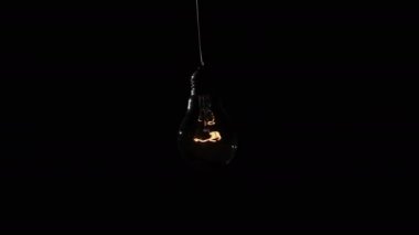Incandescent lamp lights up and flickers on black background. A light bulb turned on and off close-up. Warm flashing filament. Tungsten bulb light and cozy shine of vintage light. Idea, copy space. 4K