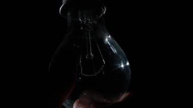 Male hand twists incandescent bulb into socket and it glows and flickers on a black background. Warm flashing filament close-up. Glass vintage light bulb glowing yellow warm light. Tungsten lamp light