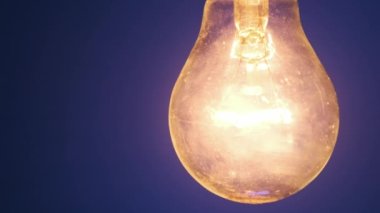 Parlayan lamba koyu mavi arka planda parlıyor ve yanıp sönüyor. Edison ampulü yavaşça açılıp kapanıyordu. Yakından yanıp sönüyordu. Ilık yanıp sönen filament. Retro klasik ampul.