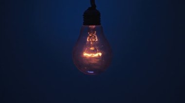 Klasik lamba koyu mavi arka planda parlıyor ve yanıp sönüyor. Edison ampulü yavaşça açılıp kapanıyordu. Yakından yanıp sönüyordu. Ilık yanıp sönen filament. Vintage Incandescent ampulü. Fikir, kopyalama alanı. 4K