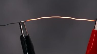 Nichrome wire heated to red under high current strength. Nichrome thread connected to power wires in a lab. Metal filament glowing, high metal resistance, short circuit. Electric power. Close-up