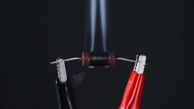 The resistor heats up with smoke under a high current strength, short circuit. An electrical component in lab burns out when exposed to high voltage. Close-up, resistance. Electric power, Ohms law.