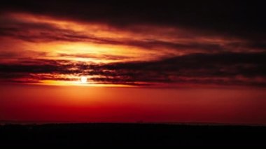 Timelapse of sunset in the orange sky behind the layered clouds over the horizon. Big bright red sun with sunrays moves down. Awesome epic cloud space, vibrant color. Time Lapse. Sundown. 4K
