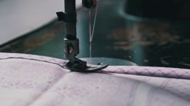 Old female hands of seamstress sew at a retro sewing machine at home in slow motion. Close-up of aged female fingers sewing fabric at a traditional sewing machine. The needle quickly moves up and down