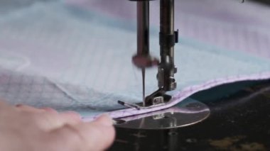 Old female hands of seamstress sew at a retro sewing machine at home in slow motion. Close-up of aged female fingers sewing fabric at a traditional sewing machine. The needle quickly moves up and down