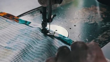 Old female hands of seamstress sew at a retro sewing machine at home in slow motion. Close-up of aged female fingers sewing fabric at a traditional sewing machine. The needle quickly moves up and down
