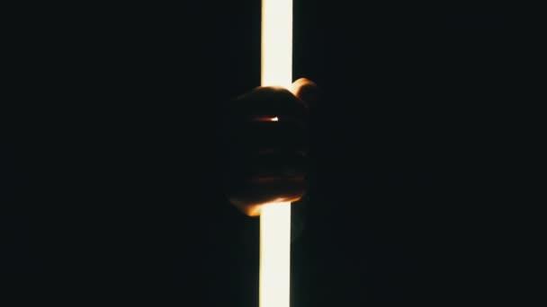 男性手拿着霓虹灯光剑 背景是黑色的 人类的手指拿着一个明亮的长Led管状灯笼 通过手电筒勾勒的手的轮廓 — 图库视频影像