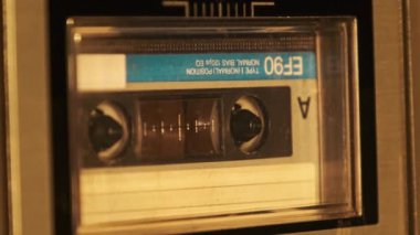 Kaset teypte çalınır. Yakın plan. Güvertede ses kaseti çalıyor ve dönüyor. Eski retro kaydediciyle klasik ses kaydı. Kaydı ara. Ses kaseti oynatılıyor. Makro