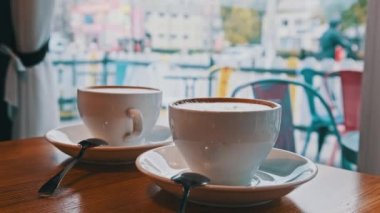 Caddeye bakan pencerenin karşısındaki kahve dükkanındaki masada. Soğuk bir sokağa bakan sıcak bir kafe atmosferi. Beyaz tabakta köpüklü iki kupa kapuçino. Şehir trafiği, insanlar