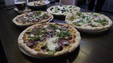 Pizzacıda bir sürü pizza var, yakın plan. Lokantada et, domuz pastırması, sucuk, peynir vb. ile iştah açıcı İtalyan pizzasından bol bol var. Çeşitli pizza çeşitleri. 4K