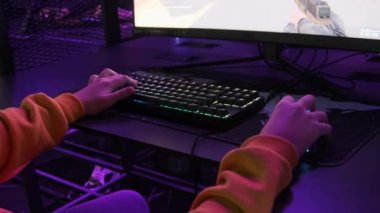 Modern Esport Kulübü 'nde gençler monitörün önünde oturur ve bir nişancı oyunu oynar. PC klavyesinde neon ışıkta duran bir çocuğun elleri görülüyor. Oyun kulübündeki gençler bilgisayar oyunları oynarlar. Sanal spor