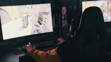 Gençler oyun kulübünde oyun sandalyesinde oturup, monitörün önünde atış oyunu oynarlar. Çevrimiçi bir turnuvada oynayan bir grup erkek arkadaş, neon ışıklı profesyonel bilgisayarların önünde oturuyorlar.