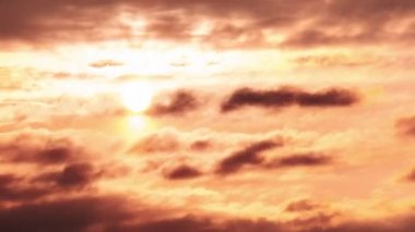 Timelapse of sunset in the orange sky behind the layered clouds over the horizon. Big bright red sun with sunrays moves down. Awesome epic cloud space, vibrant color. Time Lapse. Amazing sundown.