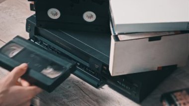 Insert VHS cassette into VCR player. Black vintage videotape cassette recorder on a desk with many archived video cassettes. Male hand inserting old VHS Tape into a retro player. Home video, nostalgia