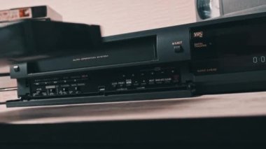 Insert VHS cassette into VCR player. Black vintage videotape cassette recorder on a desk with many archived video cassettes. Male hand inserting old VHS Tape into a retro player. Home video, nostalgia