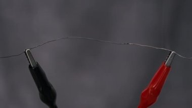 Güç kablolarına bağlı nikrome kablosu yüksek akım altında kırmızıya ısıtılır. Elektrik kabloları havayı ısıtıyor ve arka planda parlıyor. Yüksek metal direnci. Güç gücü. Kısa devre. Yakın plan.