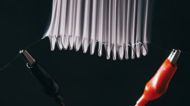 Nichrome wire heats up to red with smoke under a high electric current, slow motion. Nichrome filament in the form of spiral connected to power wires. Close-up, high metal resistance. Current strength