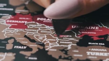 Female Hand Scratching Romania Country on the Surface of Scratch World Map. Scratch world map with Europe countries, close-up. Scratching visited countries on travel map. Erase country on scratch map