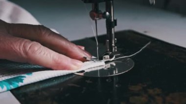 An old seamstress sews on a vintage sewing machine at home. Needle for retro sewing machine in slow motion. The process of sewing the fabric. Close-up of grandmother hands working at a sewing machine