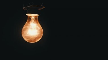 Hanging incandescent bulb turns on, and off and flickers on black background, place for text. Warm flashing filament close-up. Glass old bulb glowing yellow warm light. Tungsten lamp light. Idea 4K