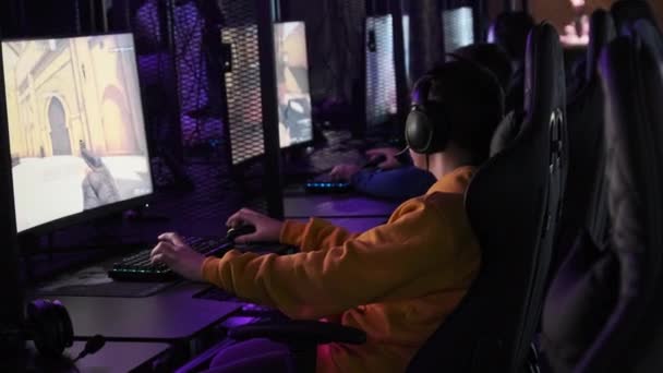 游戏俱乐部的青少年坐在监视射击游戏的游戏椅子上 一群男孩朋友坐在配备霓虹灯的专业计算机前 玩在线竞赛 — 图库视频影像