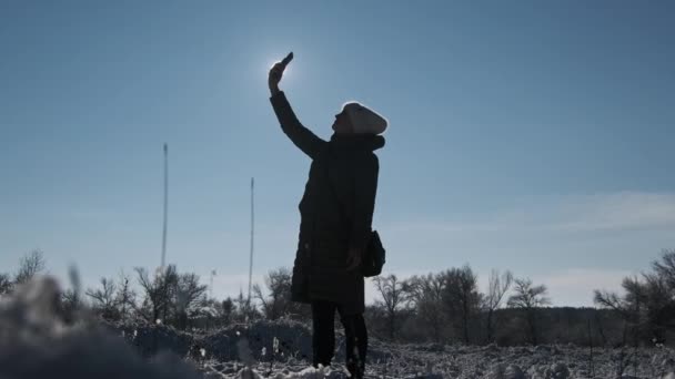 年轻女子抵御阳光时 高高地举起手 试图在冬季捕捉丢失的手机信号 智能手机遮住了太阳 通信不良 没有信号 没有移动因特网搜索信号 — 图库视频影像